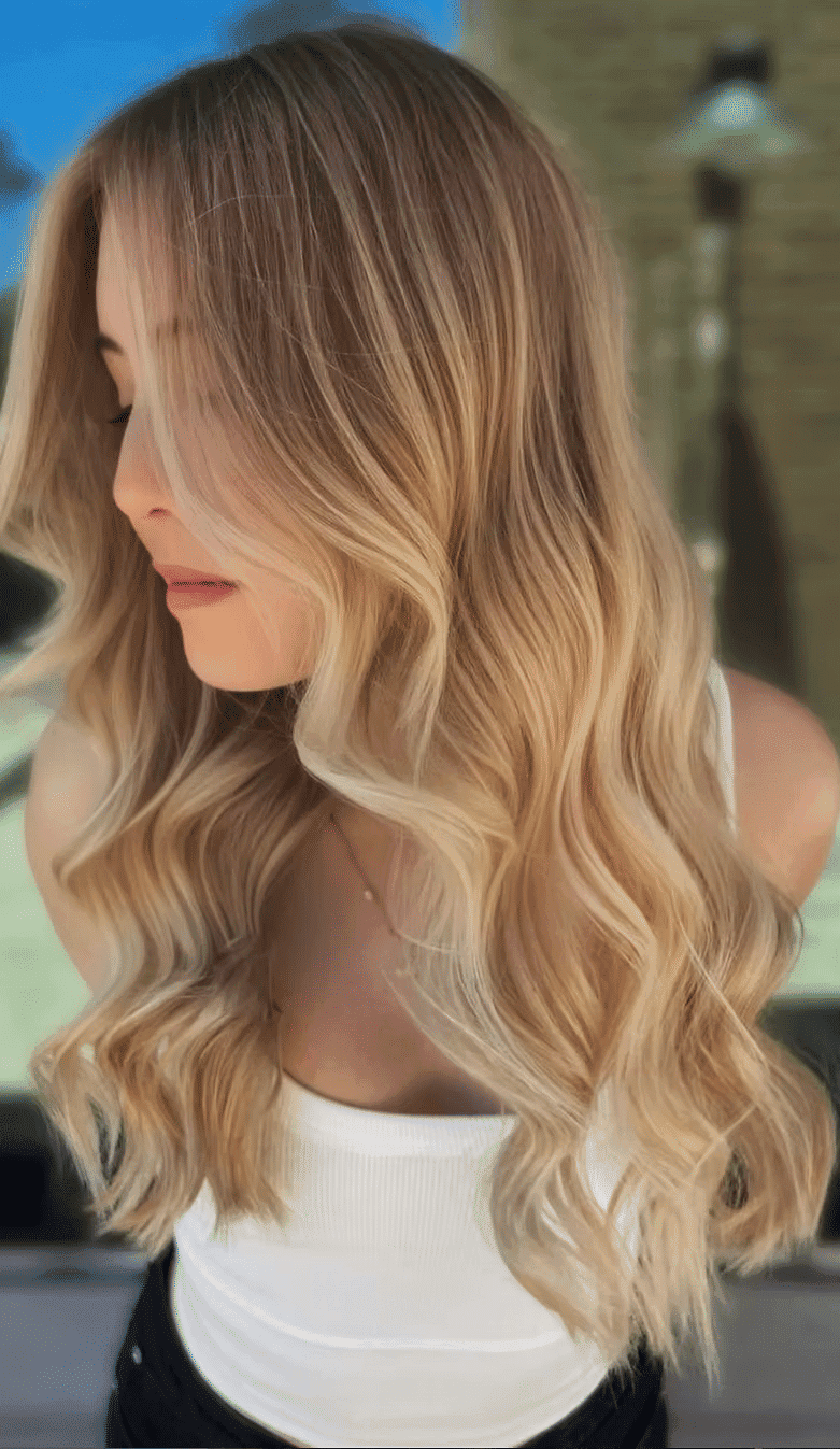 Blonde woman with long, wavy hair wearing a white top in natural light.