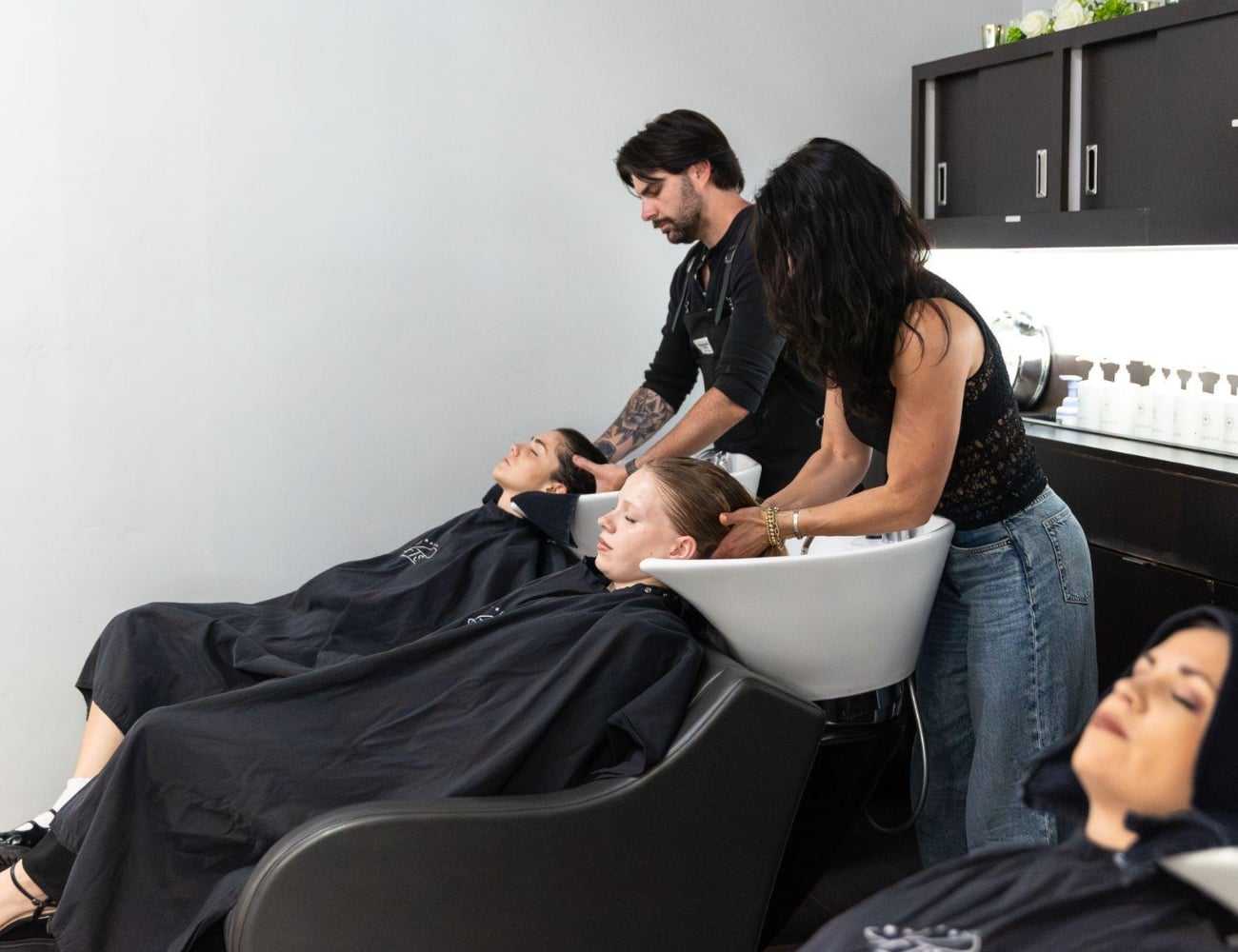 Hair salon staff washing clients' hair at modern washing stations.