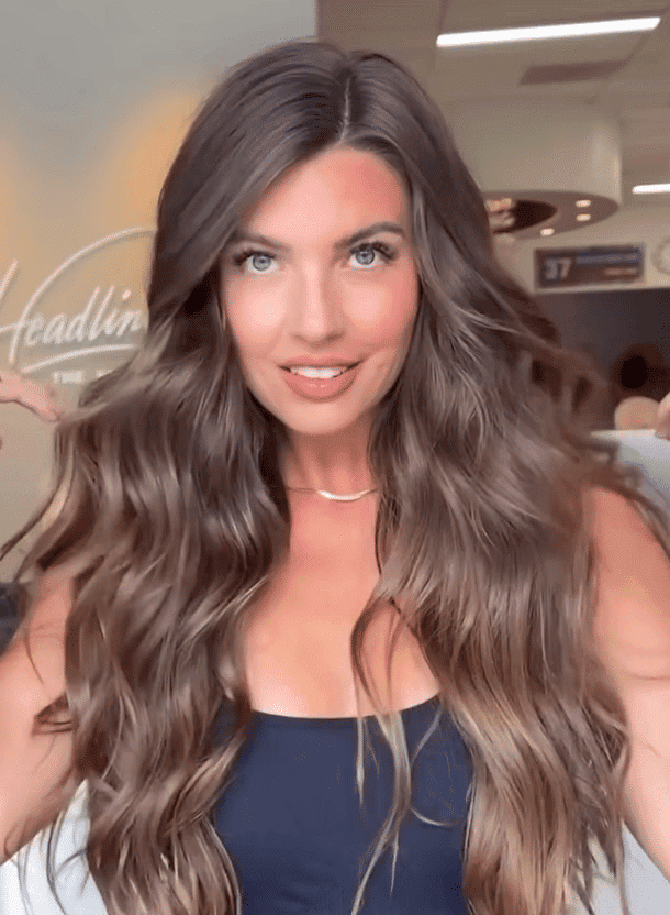Long-haired woman in salon with stylish waves and warm lighting.