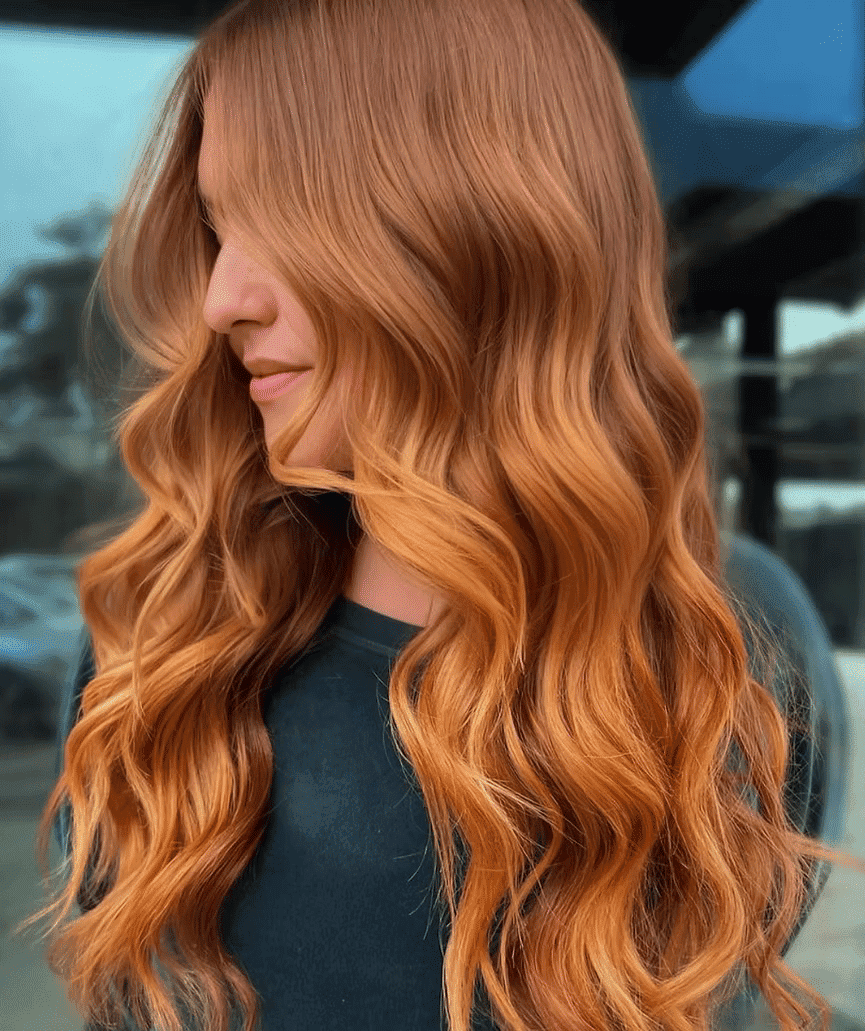 Wavy auburn hair cascading over shoulders in front of a blurred outdoor backdrop.