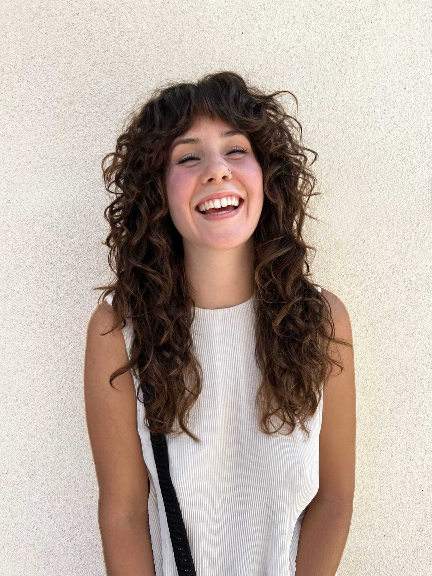 Young woman with curly hair smiling broadly against a light background.